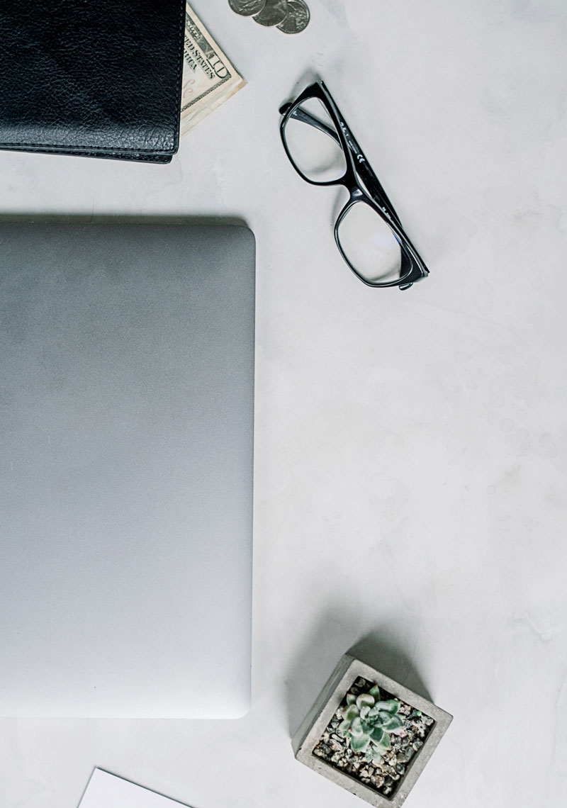 A clean desk with a laptop, wallet, and a pair of glasses